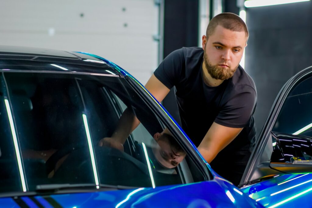 An employee of a car dealership stands at the open door of a luxury car in chameleon-colored film
