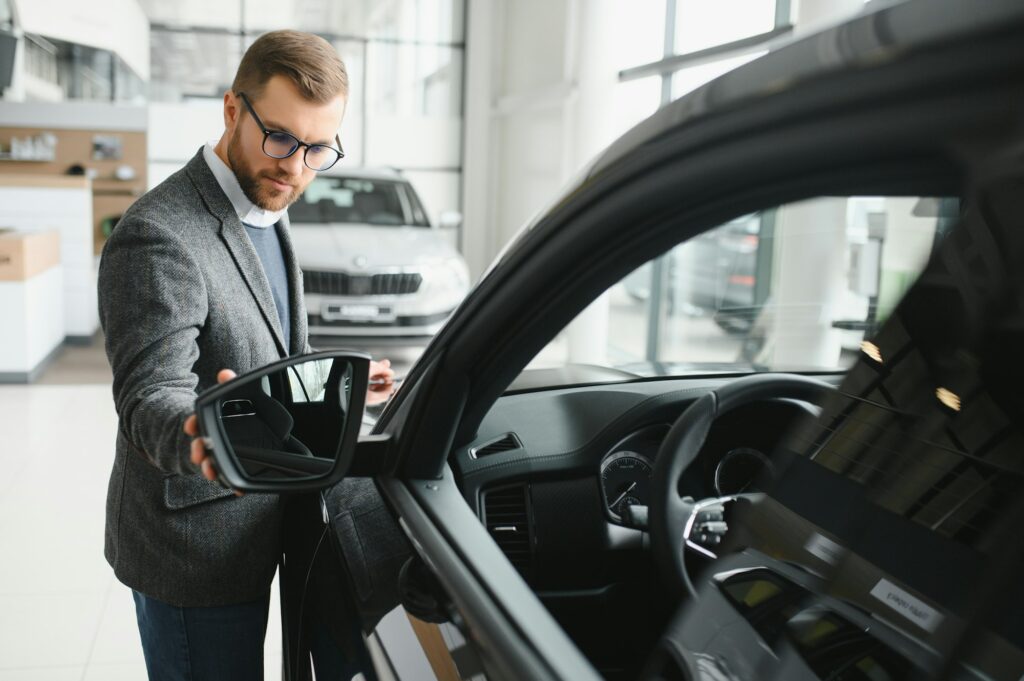 Visiting car dealership. Handsome bearded man is stroking his new car and smiling