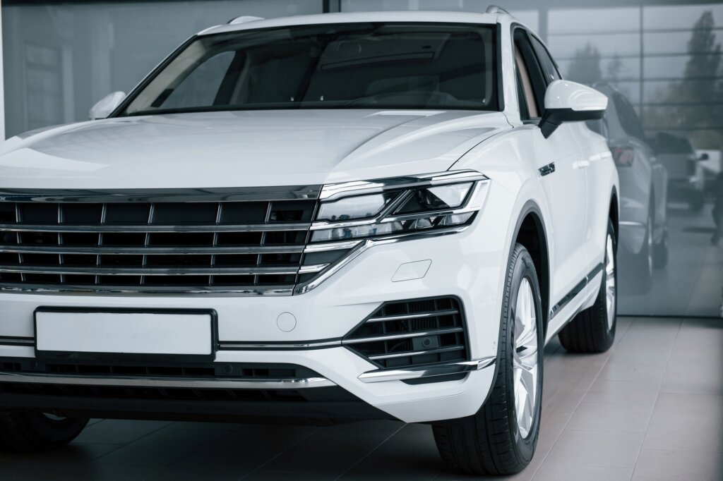 Grey glass behind. Particle view of modern luxury white car parked indoors at daytime