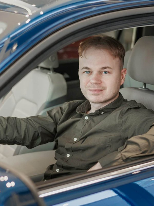 happy man is sitting in a blue car in a car dealership. a man buys a car at a car dealership