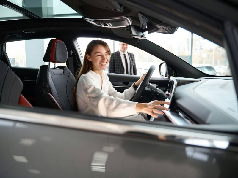 Woman choosing new car in dealership with salesman trying on new automobile