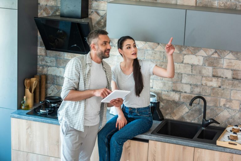 married couple with digital tablet looking away in kitchen, smart home concept